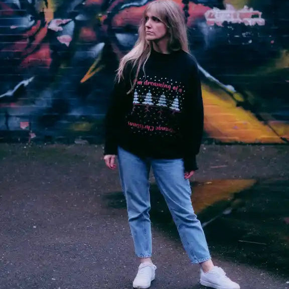 Person wearing a black sweater with text and graphics, standing in front of a colorful mural.