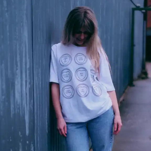 Person wearing a white t-shirt with circular graphics against a gray wall.
