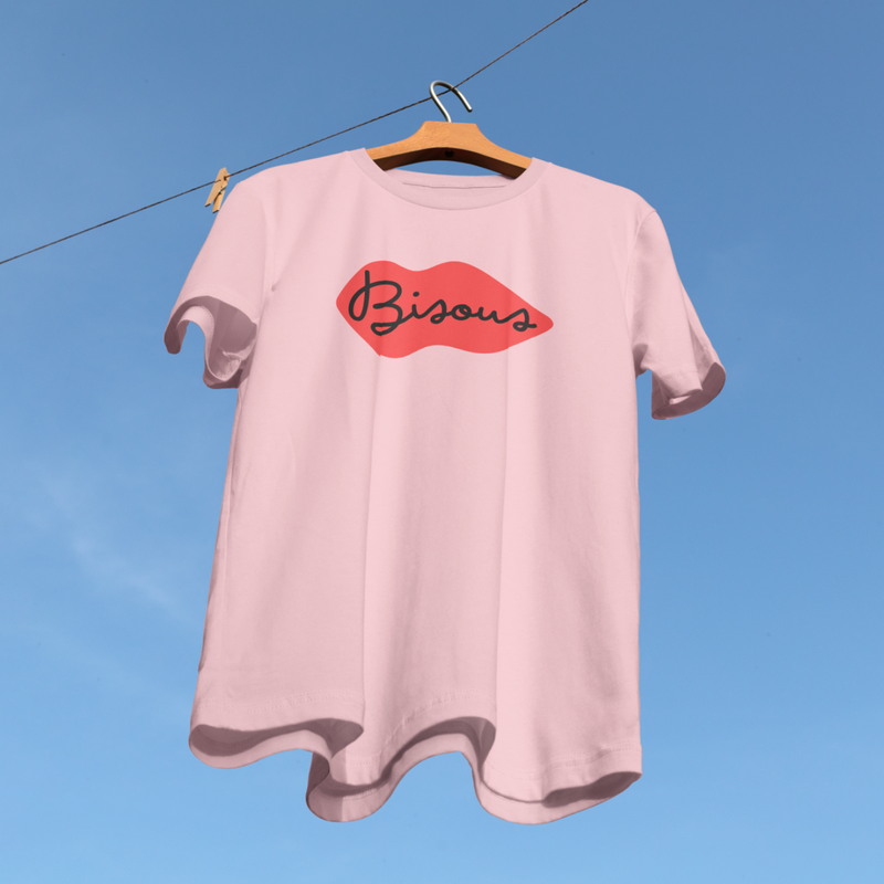 Pink t-shirt with 'Bisous' design on a hanger against a blue sky