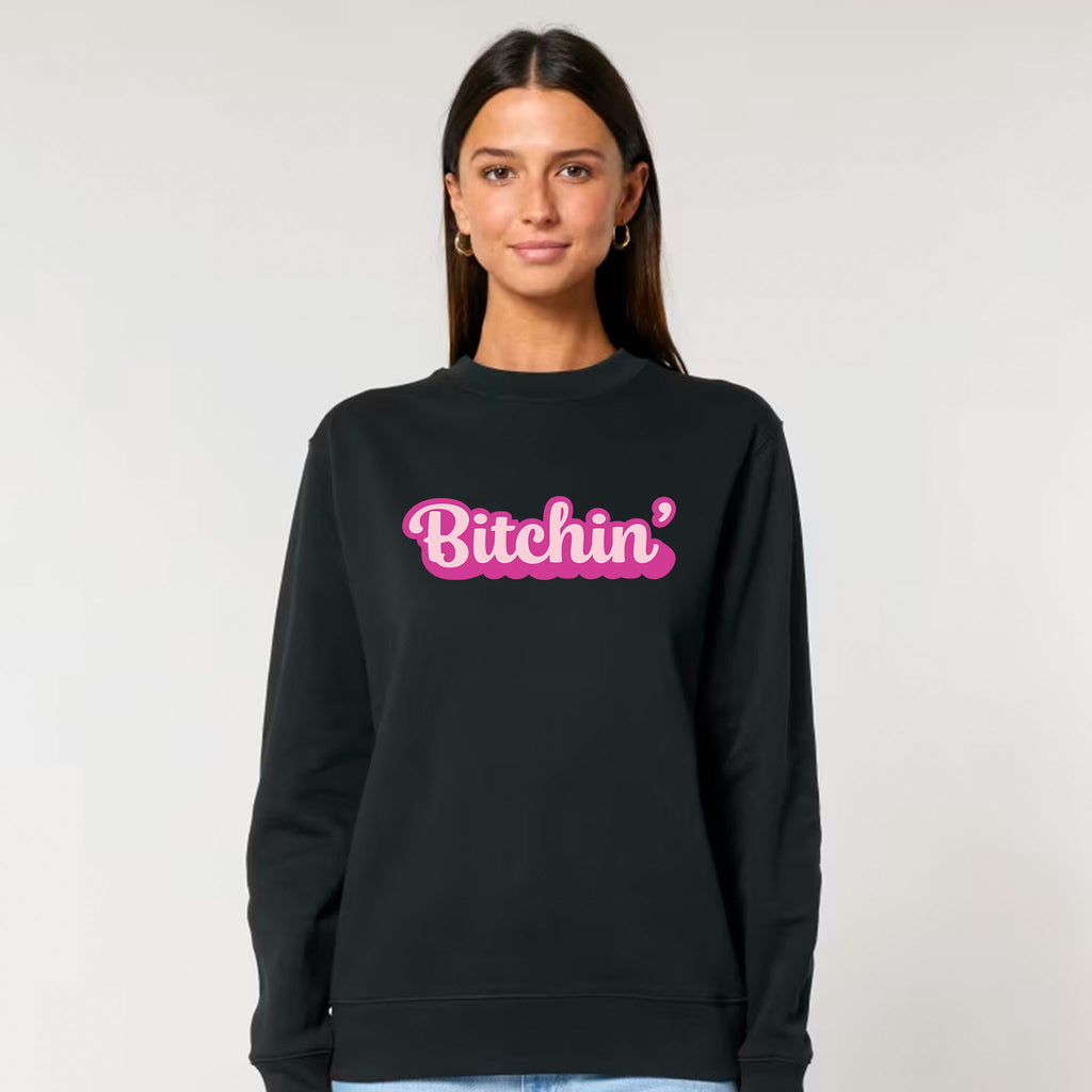 Person wearing a black cotton sweatshirt with 'Bitchin' in pink text on a plain background
