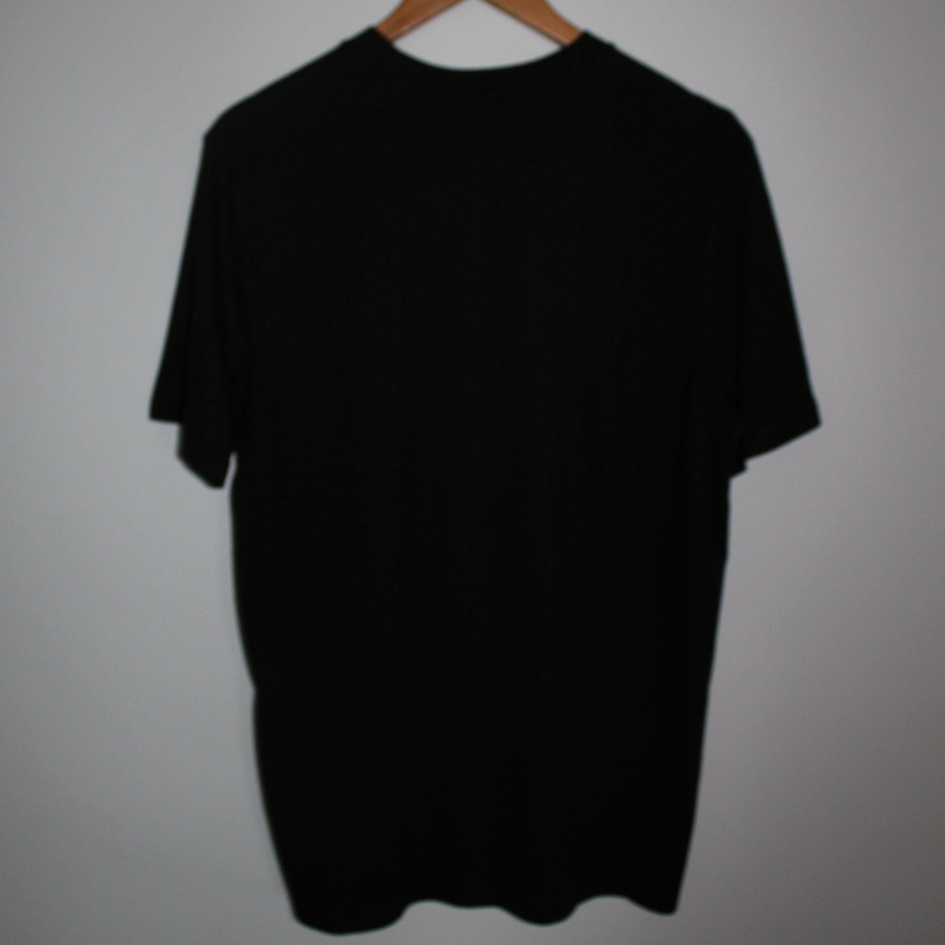Black tee on a hanger against a plain background
