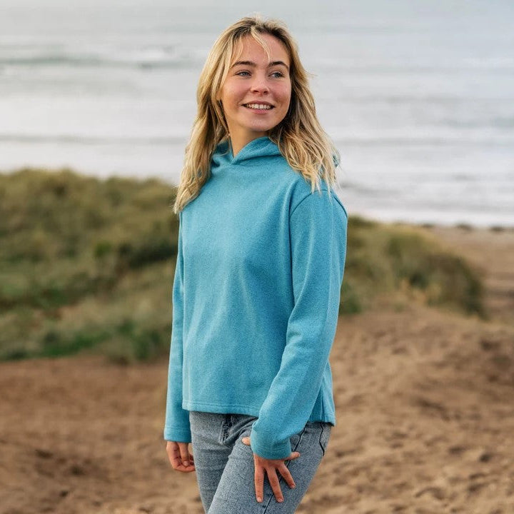 Woman wearing a blue jacket standing on a beach with ocean in the background