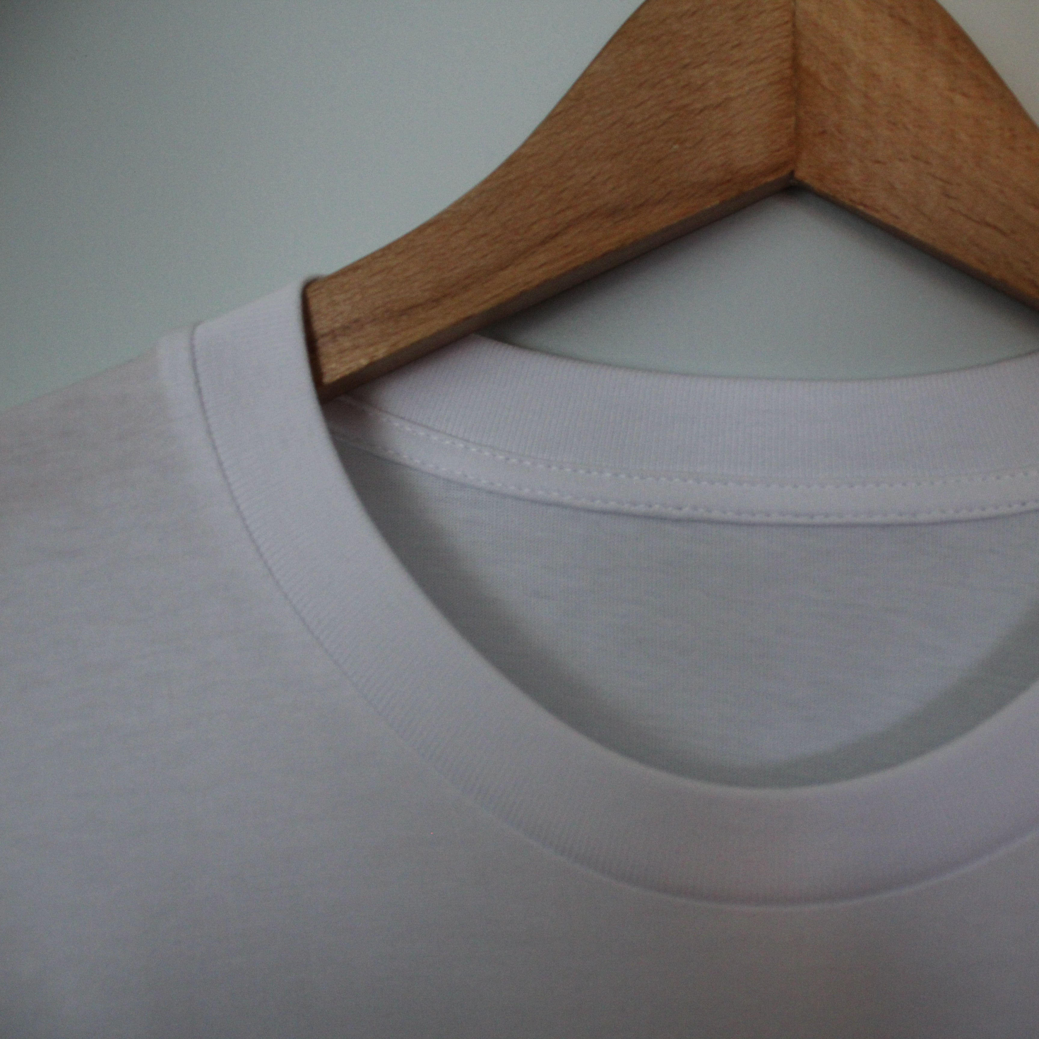 White t-shirt on a wooden hanger against a plain background