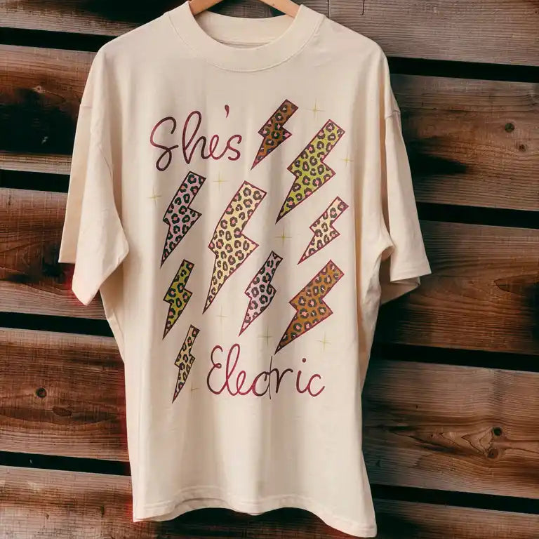 Beige t-shirt with colorful lightning bolt designs and text on a wooden background