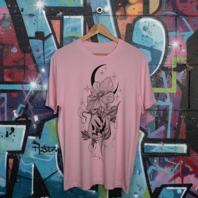 Pink t-shirt with black floral and moon design on a wooden hanger against a grafitti background