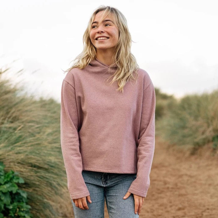 Woman wearing a pink hoodie standing in a natural setting with grass and plants.