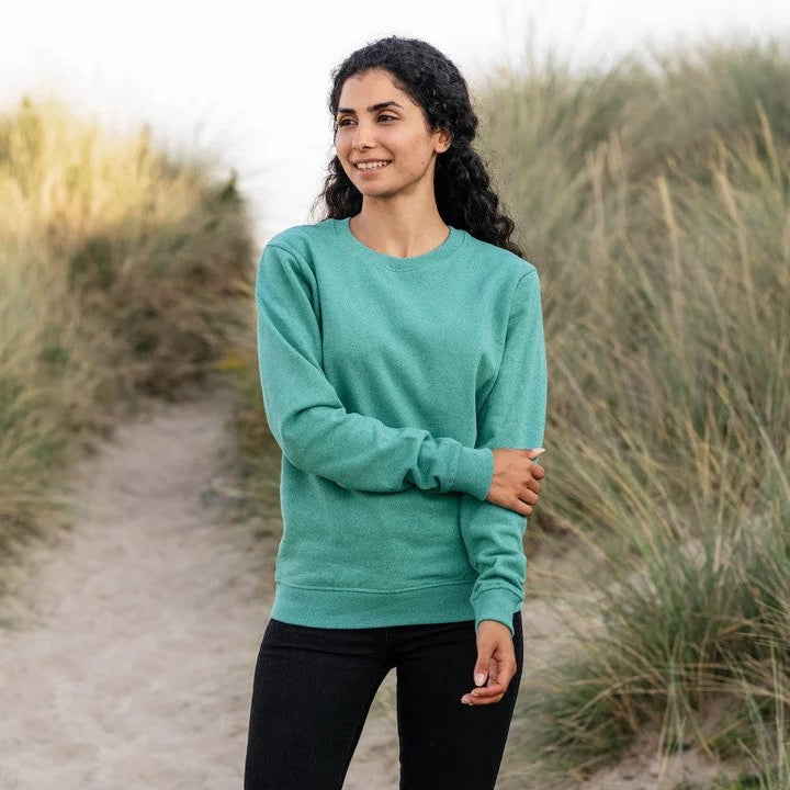 Woman in a teal sweater standing on a path surrounded by tall grass.