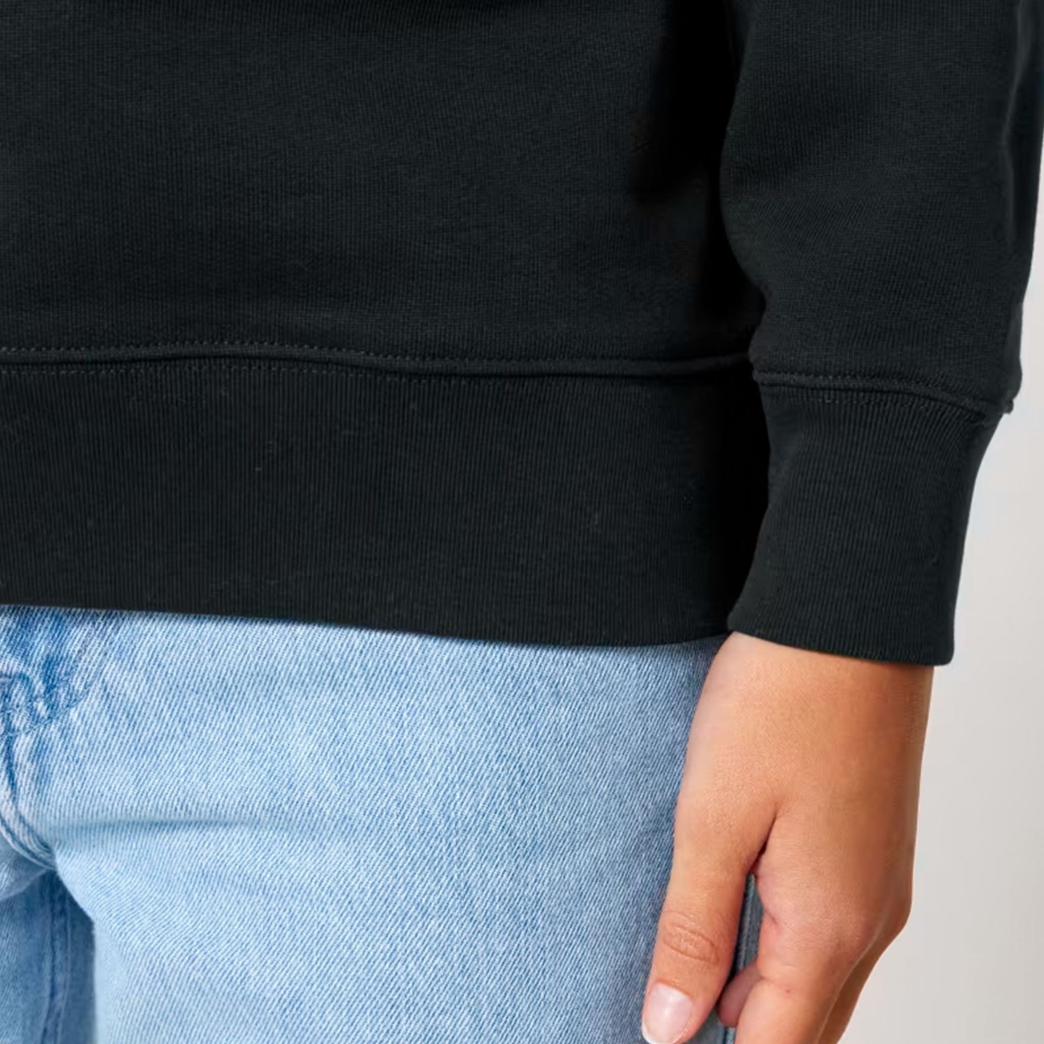 Person wearing a black hoodie and light blue jeans on a neutral background close up of sleeve and cuffed hems